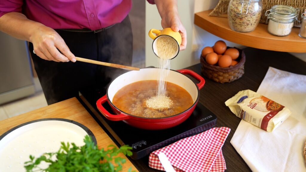 Nesta etapa crucial das pataniscas de bacalhau com arroz de feijão, coloque o caldo de carne, os temperos e o arroz no tacho